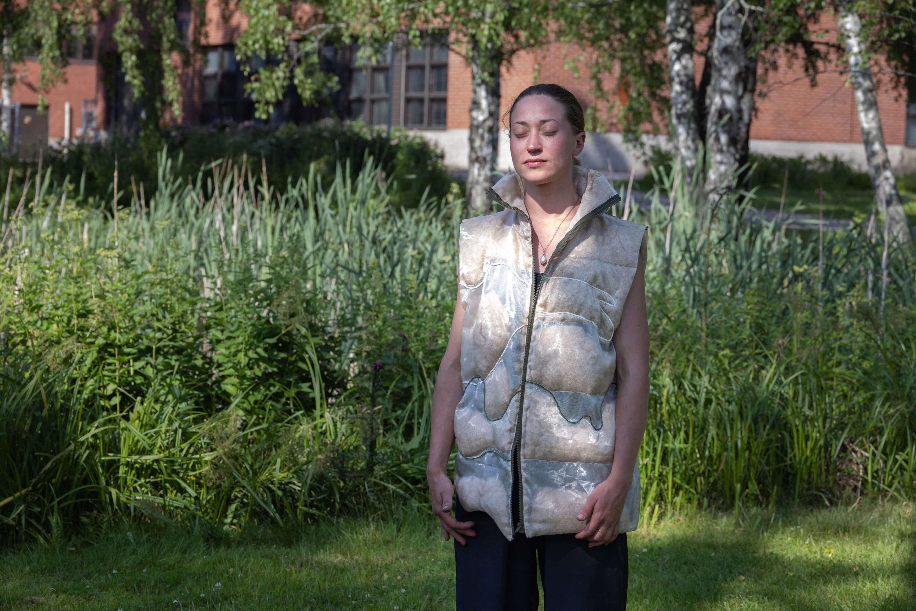 A woman with closed eyes wearing a vest filled with cattail fluff.