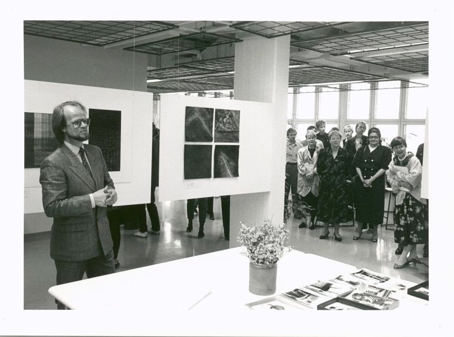 Exhibition space with people gathered around speaker and art work.