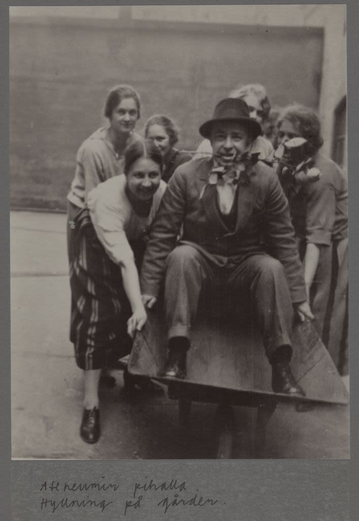 Six people posing together with a man in the middle in a suit and hat with a rose in his mouth.