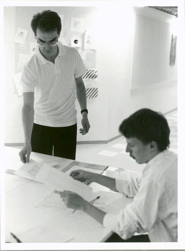 Two men at a table looking through papers.