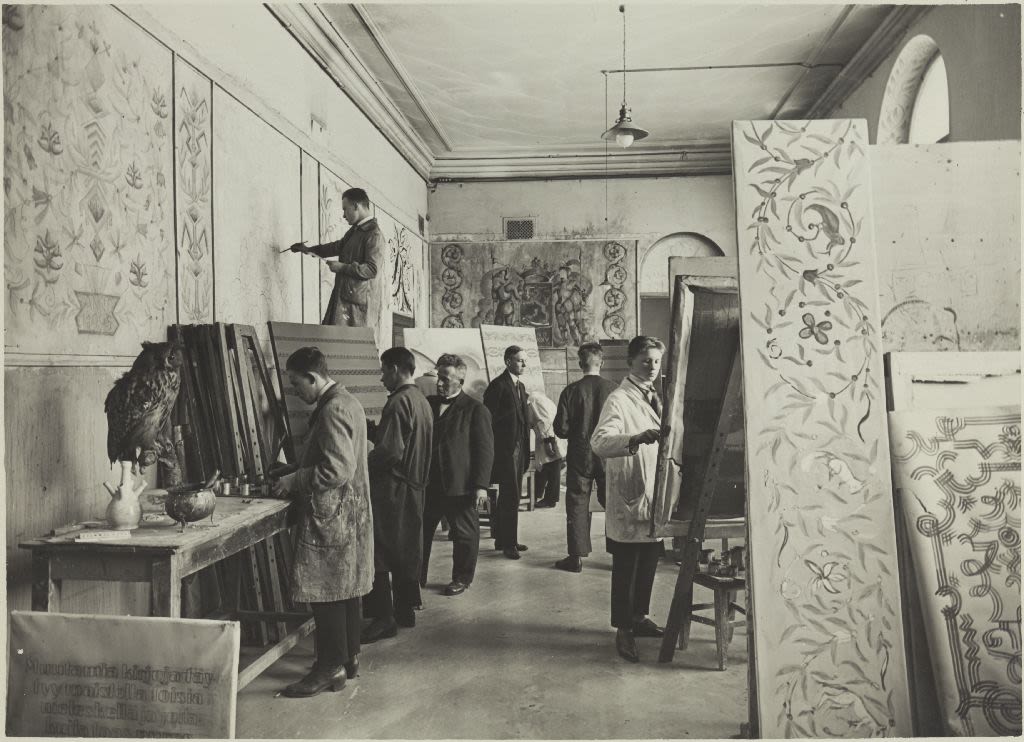 Seven people painting a classroom wall with paintings around them