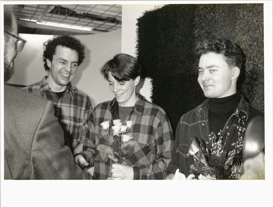Three smiling people with flowers.