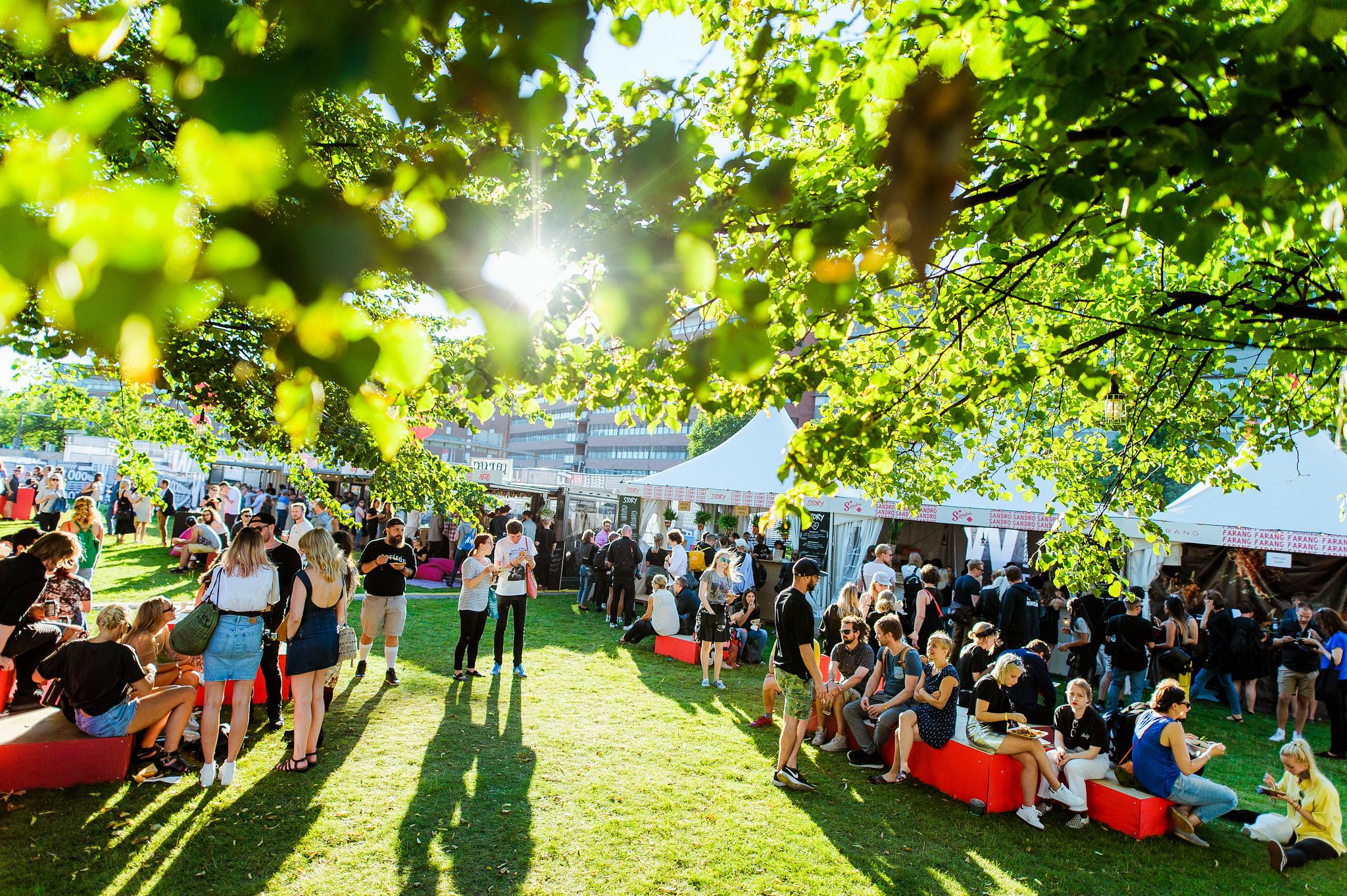 Festival goers in green oasis with white tents and crates for seating