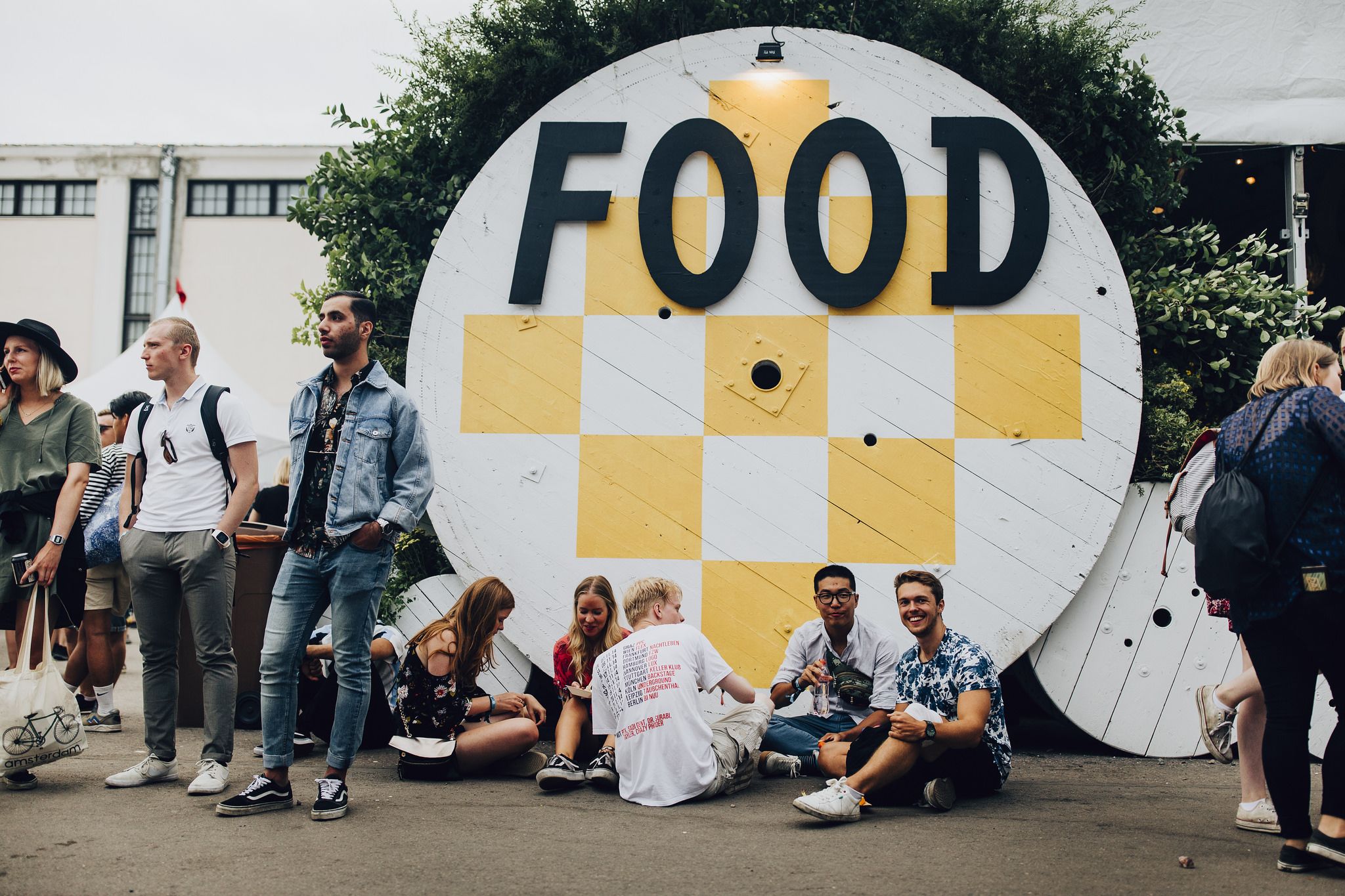 Festivalgoers in from of wooden circle in white and yellow with "Food"written on it.