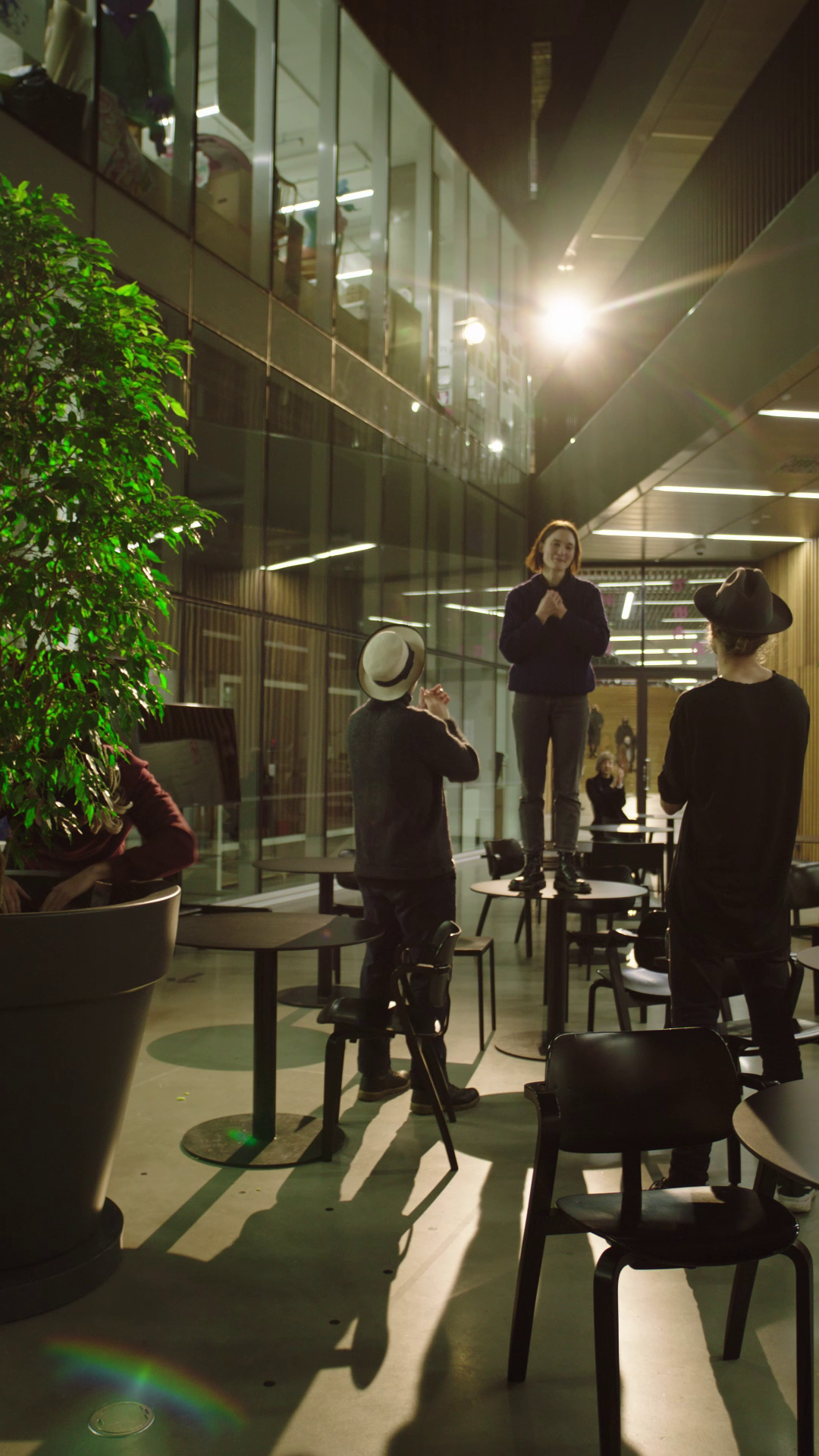 one person standing on the table clapping her hand with two men looking up at her