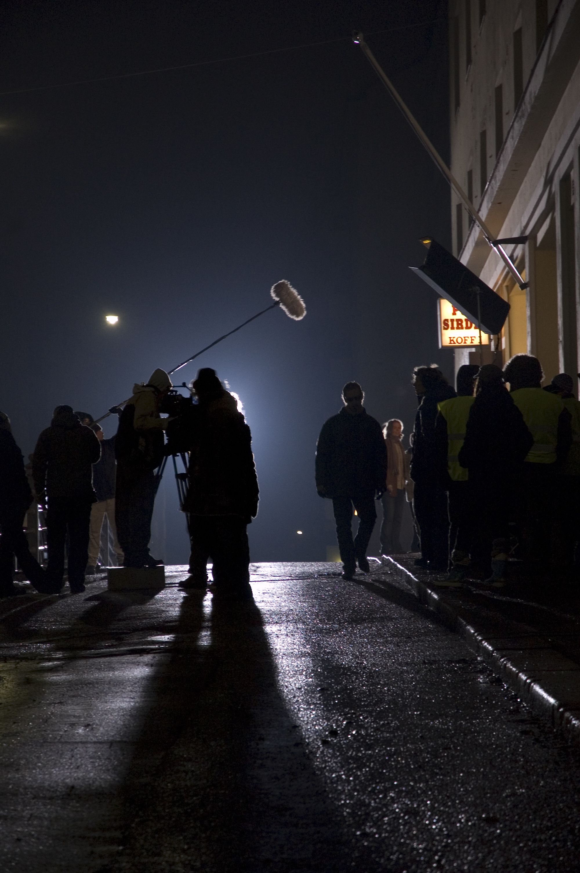 film set during night time with wet asphalt and people walking