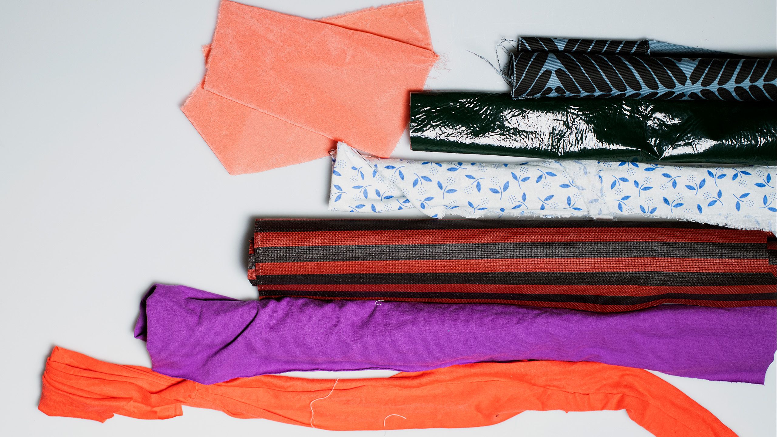 korallin, oranssin, liilan, musta-punaraidallisen, valko-sinikuvioisen ja mustan värisiä tekstiilirullia 